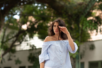 Beautiful young dark haired woman looking over her shoulder in a green street of a city