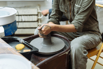 The girl sits at the Potter's wheel and creates a pot of ceramics. A Potter makes pottery out of clay behind a mechanical circle.