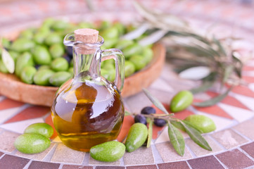 Fresh green olives with branches and leaves. Seasonal harvest in Italy. Bottle of olive oil and...