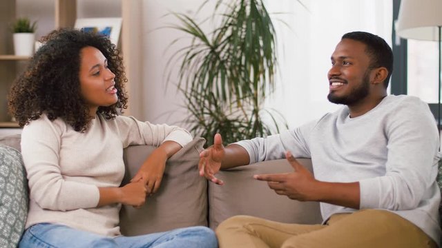 communication, relationships and people concept - happy couple sitting on sofa and talking at home