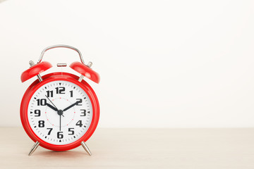 Red retro alarm clock, with a large dial on a wooden table on a white background. The concept of time, delay, morning rise, the appointed meeting. Layout with copy space for your text.