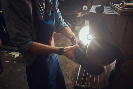 Hands of shoe master, which is working on shoe sole, using special machine tool.