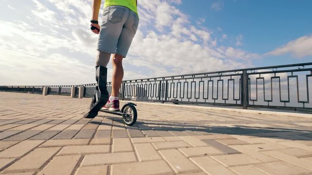 Disabled man with an artificial leg is riding a scooter in slow motion