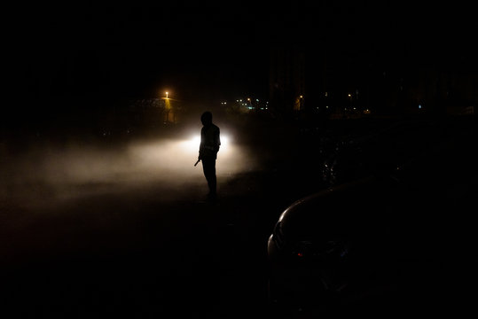 Silhouette of unrecognizable man illuminated by the headlights of a car on a dark night.