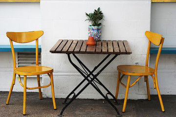 Fototapeta na wymiar Yellow chairs and outdoor wooden table by the rough white wall decorate with small plant on the table