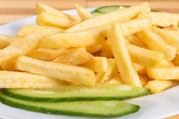 French fries, on a plate, with a cucumber.