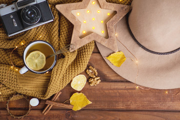 flat lay in autumn style concept cosiness, sweater, retro camera, hat, vintage, mug with hot tea, lemon and cinnamon in a cozy house. Against the background of a dark wood table