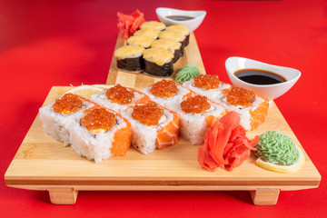 Sushi, with curd cheese, salmon and caviar. On the plank. On a red background.