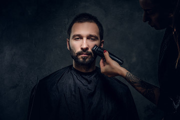 Handsome man gets a hair care from tattooed female hairdresser at dark studio.