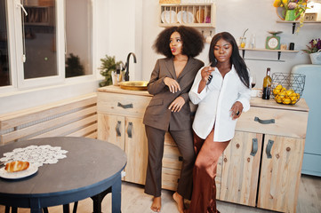 Two african american female friends women spending time at kitchen with wine. Black girlfriends  relaxing at home and eat chocolate.