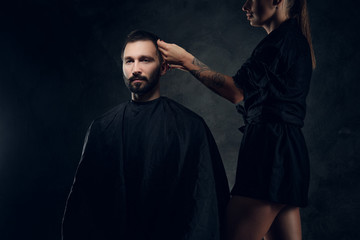 Handsome man gets a hair care from tattooed female hairdresser at dark studio.