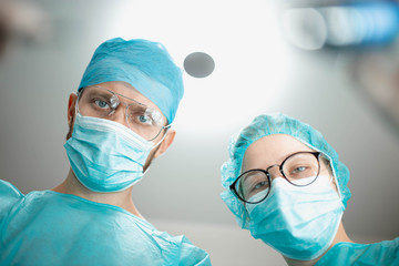 Professional surgeon with a young female assistant intern in a hospital operating room. Shot from a lower angle, surgery.