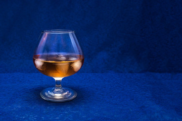Glass of alcohol, whiskey with ice on a blue background.