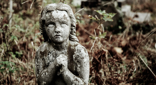 Ancient statue of a praying angel with broken wings as symbol of pain.
