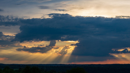 Dramatic sunset sky with sunbeams behind clouds in Neudenau, Germany