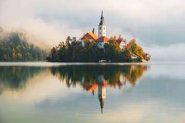 Famous Bled Lake in Triglav National Park in the Julian Alps with a forest in autumn colors at sunrise - 302087632