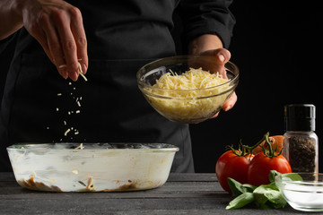 The chef cooks Italian lasagna, sprinkled with mozzarella. Freeze in motion