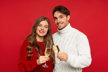 smiling couple clinking champagne glasses and looking at camera isolated on red background. Christmas concept
