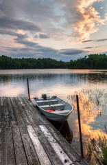 fishing boat and motor tied at old wooden dock with sunset and calm water