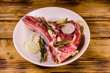 Raw ribeye steak, spices, rosemary, onion and garlic in a ceramic plate on wooden table