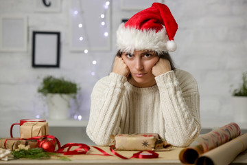 Depressed frustrated woman wrapping Christmas gift boxes, winter holiday stress concept