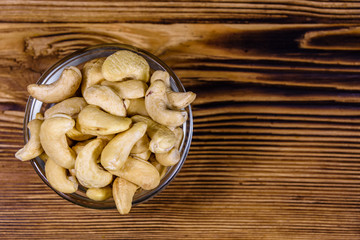Glass bowl with raw cashew nuts on a wooden table. Top view