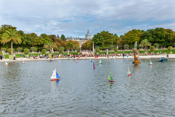 Fototapeta na wymiar Multi-colored boats float in a pool around a fountain in Luxembourg Park. August 5, 2019. Paris. France.