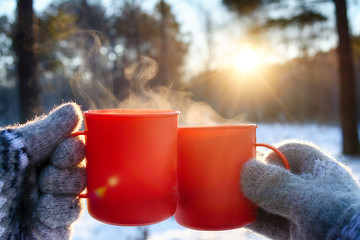 young man and young woman in knitted wool mittens with mugs of hot drink on sunny frosty day on...