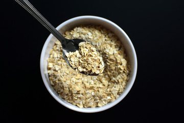 Bowl of raw oatmeal on black background