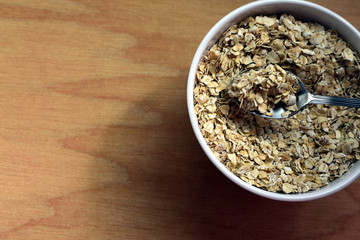 Bowl of raw oatmeal with spoon on wooden background
