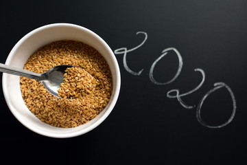 Bowl of flexseeds with spoon on black background with number 2020 from above