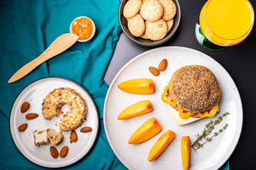 Homemade breakfast: sandwich with cheese and ham, cream cheese, almond, persimmon, jam and orange juice. Top view, flat-lay