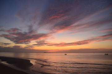 A bright orange coloured tropical cloudy coastal sunrise seascape in a blue sky. Thailand.