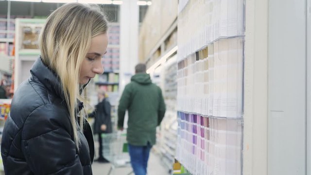 Woman choosing color of wall paint in decoration department of hardware store