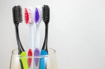 multi-colored toothbrushes in a glass on a light background