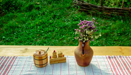 Ukrainian traditional folk still life photography after dinner clay flower vase and wooden saltpeter on table with table cloth on unfocused green grass background in back yard garden space