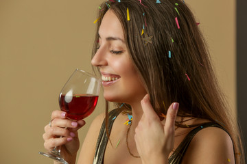 Attractive woman in golden shirt dancing and holding a glass of red wine. Happy young and beautiful woman enjoying the party with confetti.