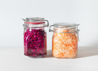 Homemade sauerkraut with carrots and cabbage salad with beets in a glass jar on a white wooden background. Fermented food.