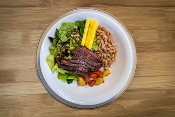Beef with beans, grilled vegetables and salad on a wooden background. Top view