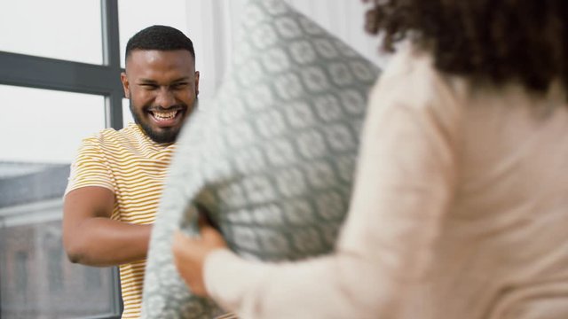 moving, people, repair and real estate concept - happy african american couple having pillow fight at new home