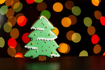 gingerbread cookie of green christmas tree over defocused colored lights of garland. Traditional Christmas food. Christmas and New Year holiday concept.