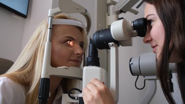 Smiling oculist is starting to check an eye sight of young happy woman. Camera man is coming closer, and after he is moving back.