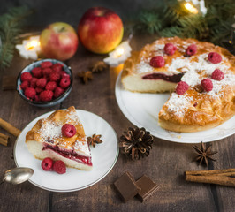 Delicious Christmas raspberry pie with berry filling and icing sugar and spices on a dark background.