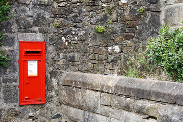 Red post box embed in weathered stone wall in United Kingdom