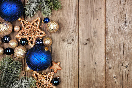 Christmas Side Border With Dark Blue And Gold Ornaments And Tree Branches. Top View On A Rustic Wood Background.