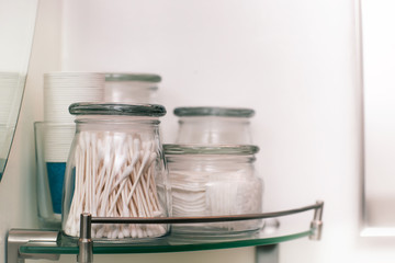 Makeup remover pads and cotton swabs on a modern glass shelf.