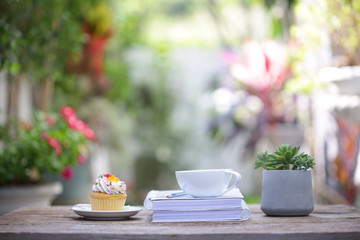 White coffee cup with cupcake  and small plant and diary notebook on wooden table at outdoor
