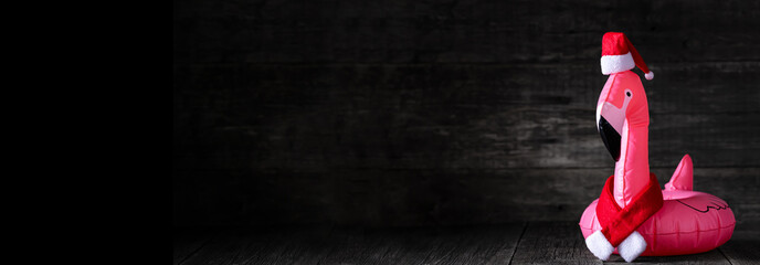 Inflatable pink flamingo in Santa Claus hat and red scarf on wooden rustic background © photopixel