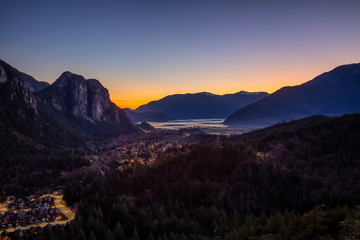Squamish, North of Vancouver, British Columbia, Canada. Beautiful Aerial View from the top of the Mountain of a small town surrounded by Canadian Nature during Autumn Sunset.
