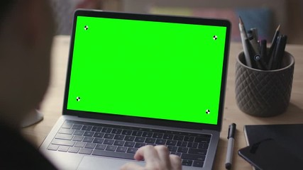 Over the shoulder shot of young woman working on modern laptop with green screen mock-up. Hands on keyboard. - Powered by Adobe